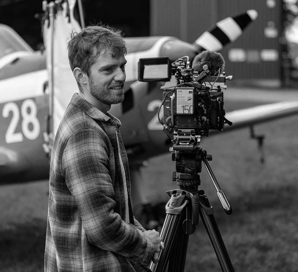 Camera operator stood alongside cinema camera on tripod